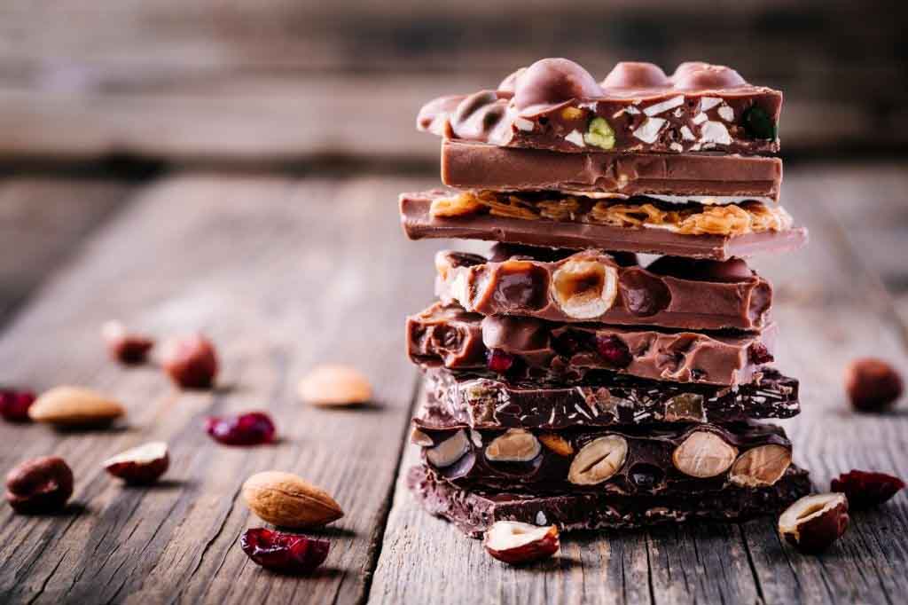 Stack of milk and dark chocolate with nuts, caramel and fruits and berries on wooden rustic background.