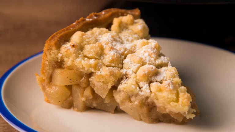 Porción de tarta de manzana con cobertura crujiente y azúcar espolvoreado en un plato blanco.