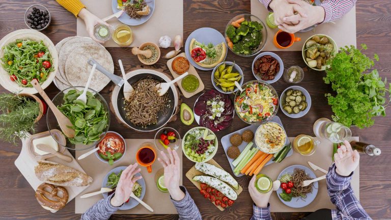 Vista cenital de una mesa compartida con ensaladas, verduras, pan, hummus y varios cuencos de comida.