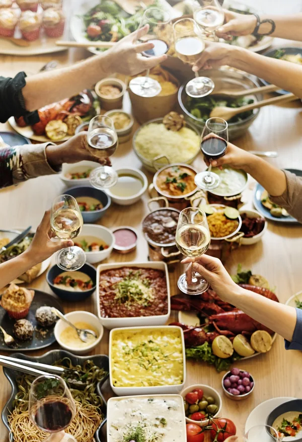Varias personas brindan alrededor de una mesa con platos para compartir, vista desde arriba.