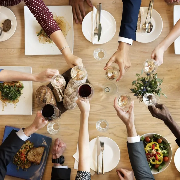 Personas sentadas a una mesa de madera brindan con copas durante una comida de grupo.